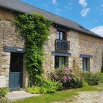 Vue de la cour pavée du gîte 15 personnes Ker Bara du Domaine de Beauregard en pierre, avec portail en bois donnant sur un jardin fleuri, situé en Bretagne.